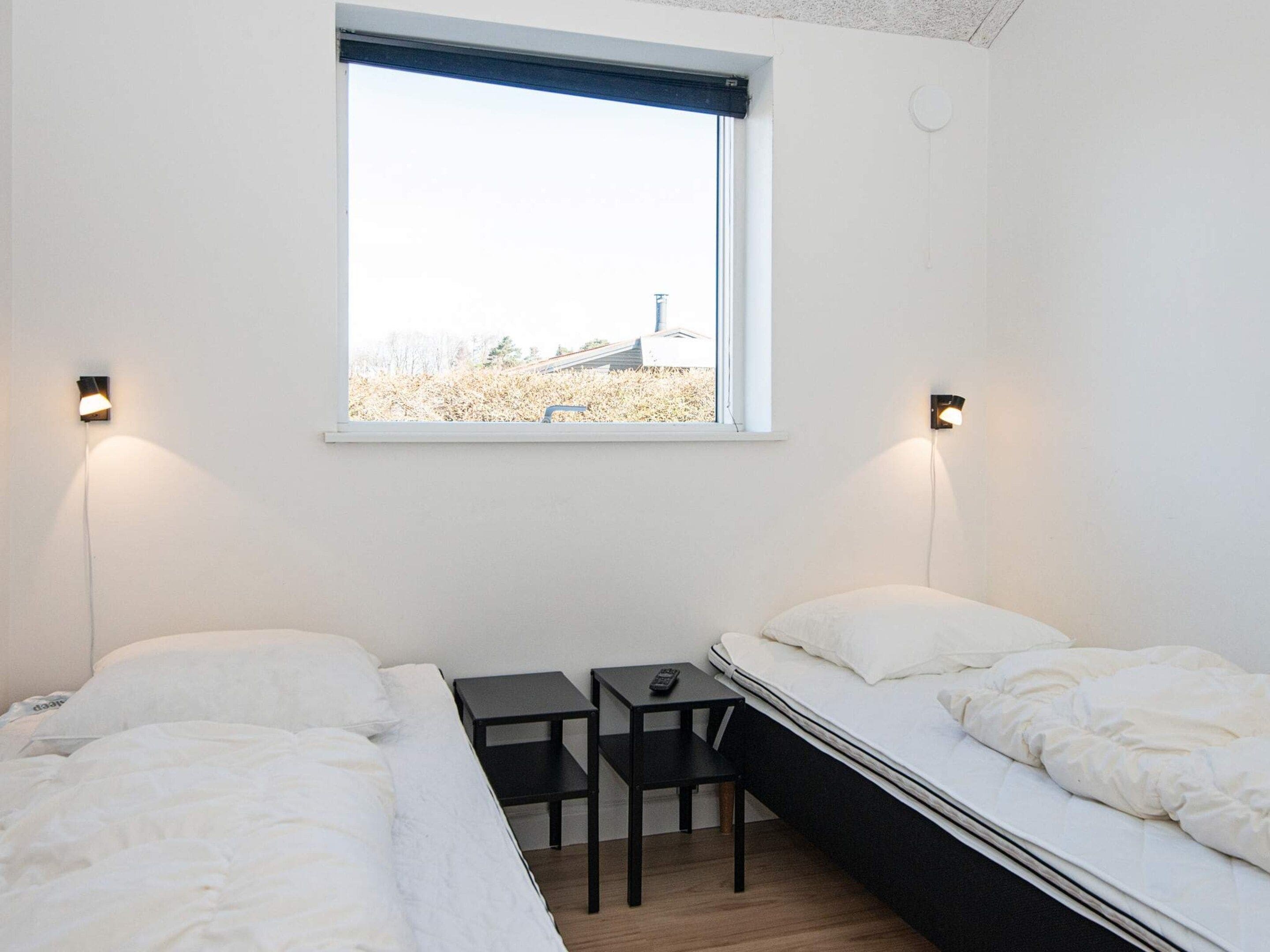 Ett sovrum med två sängar, ett litet bord, en stol och ett fönster med utsikt över en byggnad och träd.