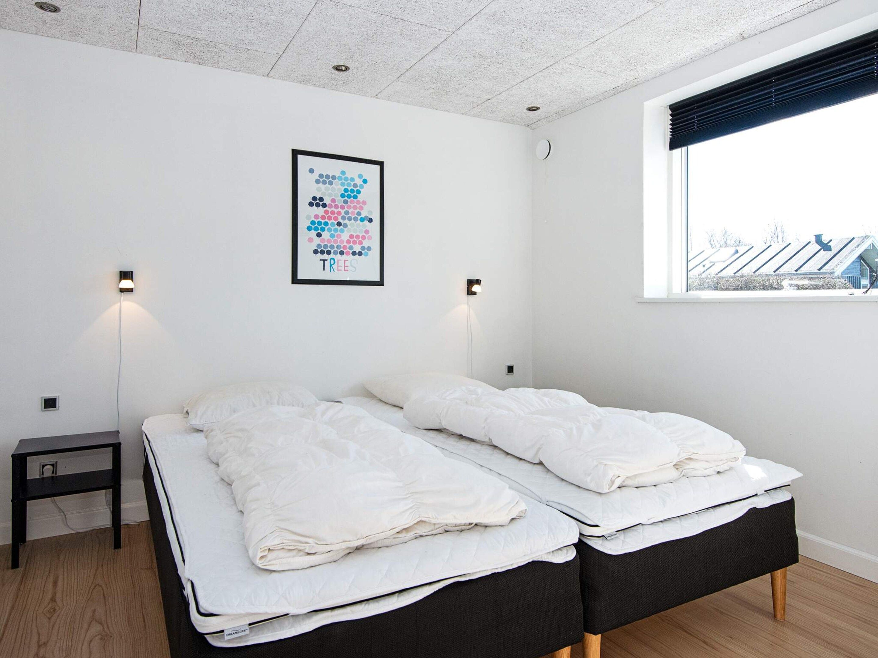 Un dormitorio con dos camas, una mesita de noche, una lámpara de pared y una ventana con vista a edificios.