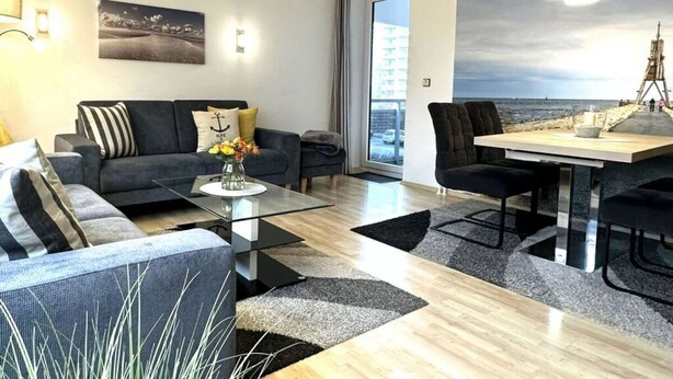 Un salon moderne avec un canapé, une table basse et un coin repas. Une grande fenêtre offre une vue sur la mer et un immeuble.
