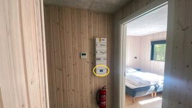 Une pièce aux murs en bois, avec un extincteur, un lit et une fenêtre.