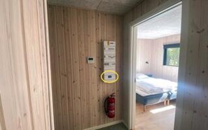 A room with wooden walls, a fire extinguisher, a bed, and a window.