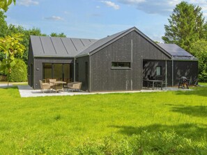 A modern house with a large patio area, a dining table, and a barbecue setup. - 4 Star Holiday Home in Glesborg (Glesborg)