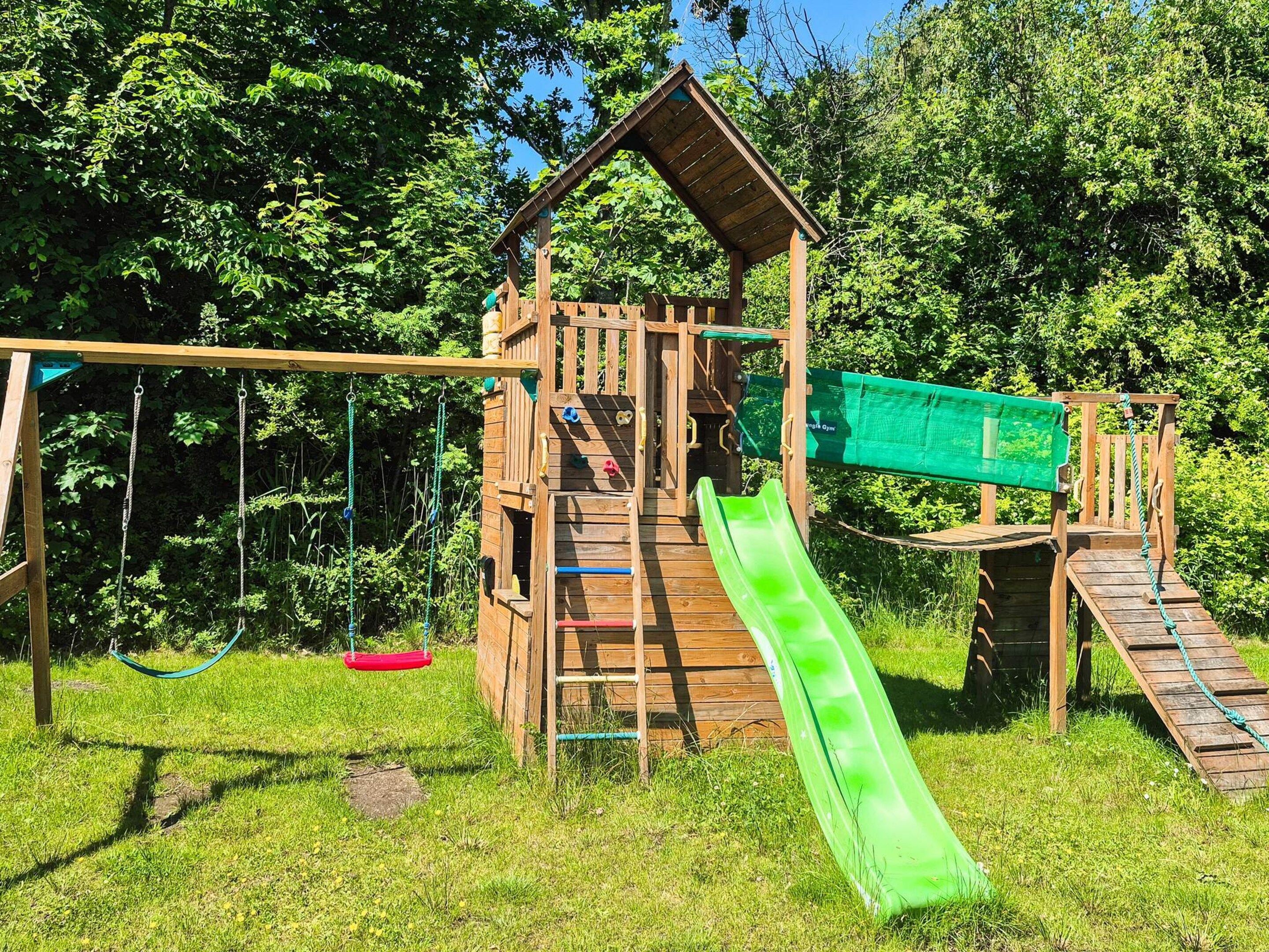 A wooden playground structure with a slide, swings, and climbing elements.