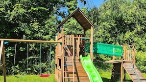 Une structure de jeux en bois comprenant un toboggan, des balançoires et des éléments d’escalade.