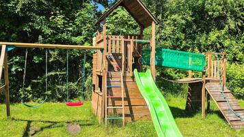 A wooden playground structure with a slide, swings, and climbing elements.