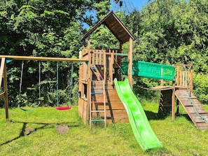 A wooden playground structure with a slide, swings, and climbing elements.