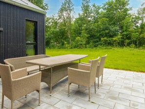 Eine Terrassengruppe mit Tisch und Stühlen, ein dunkles Gebäude im Hintergrund und eine grüne Fläche mit Bäumen.