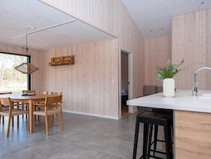 A modern kitchen with wooden panel walls, a dining area with a round table and chairs, and a view through an open door.