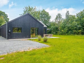 A modern building with a dark exterior, a gravel driveway, and a grassy yard.
