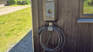 Une borne de recharge pour véhicules électriques astucieuse, fixée à un mur en bois et dotée d’un tuyau.