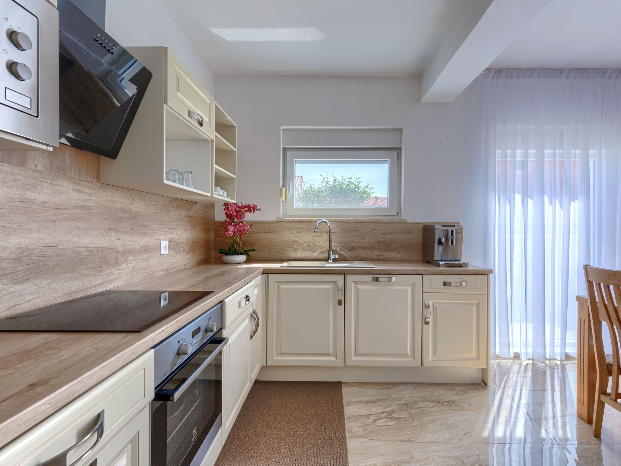 A modern kitchen with a built-in oven, a sink, and a window above the countertop.