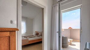 Une chambre à coucher avec un lit, une tête de lit en bois, une fenêtre avec des rideaux et une vue sur le balcon extérieur.