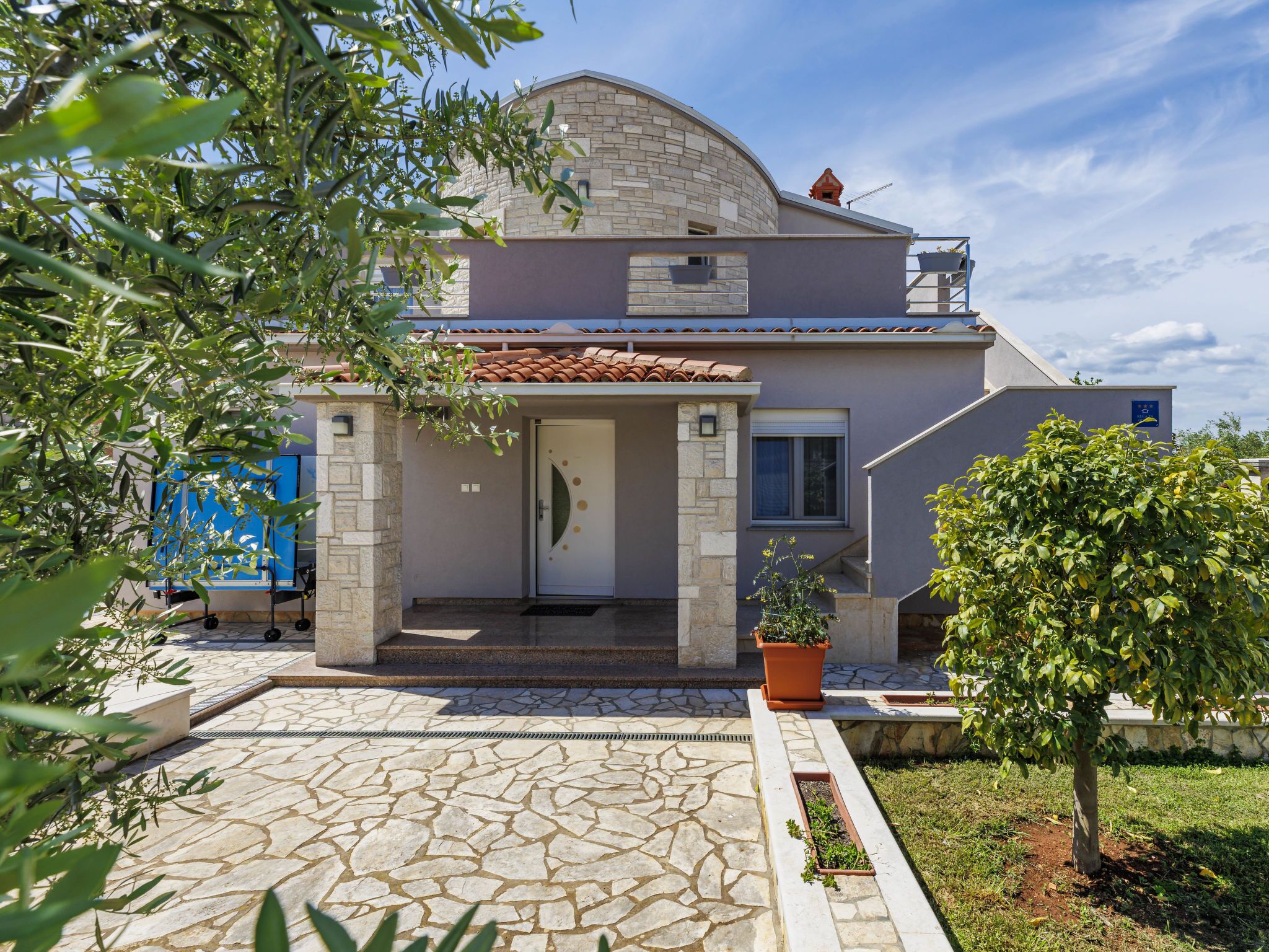 Une maison à deux étages avec une façade en pierre, un toit en tuiles et une entrée pavée de pierres.
