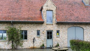 A stone building with a red-tiled roof, a wooden table and benches in the front, and a paved pathway leading to the entrance. - Comfortable Home for a Group With a Large Garden (Diksmuide)