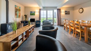 A cozy room with a fireplace, a television, a dining area with wooden chairs, and a view through a glass door. - Comfortable Home for a Group With a Large Garden (Diksmuide)