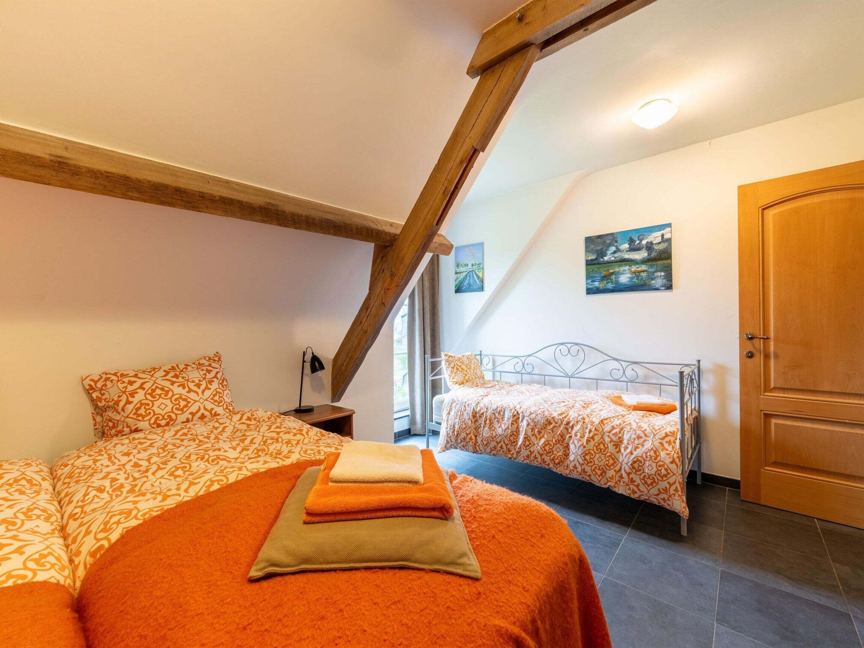 Een slaapkamer met twee bedden, houten balken, een deur en een schilderij aan de muur.