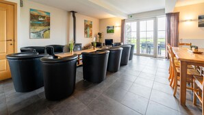 A spacious room with a long wooden table and chairs, a fireplace, and several black stools. - Comfortable Home for a Group With a Large Garden (Diksmuide)