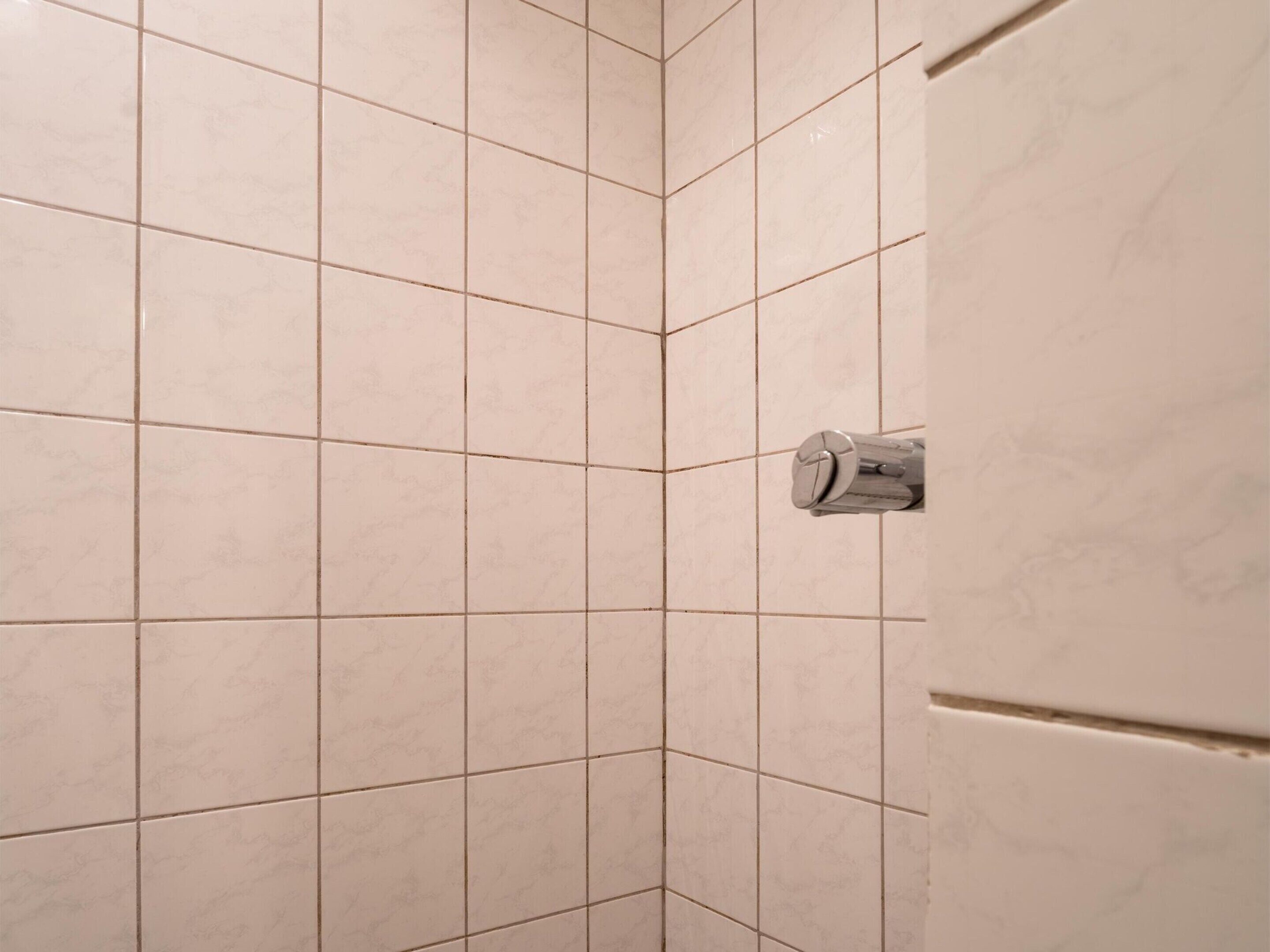 Une zone de douche carrelée avec un pommeau de douche placé dans un coin.