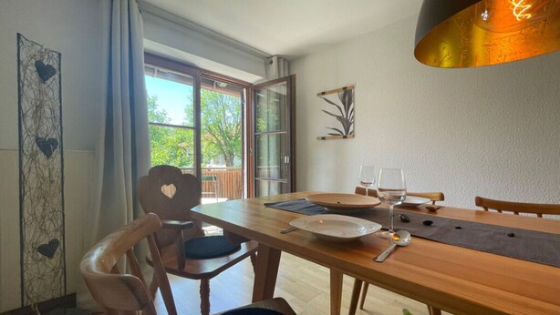 A dining area with a wooden table, chairs, and a view of the outdoors through large windows. - Holiday Apartment Lucky guy (Oberstaufen)