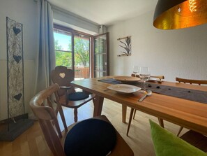 Ein Essbereich mit Holztisch, Stühlen und Blick ins Freie durch große Fenster.