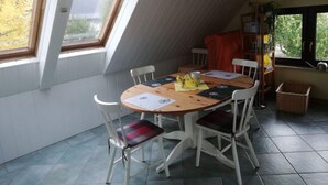 A dining area with a wooden table and white chairs, large windows, and a bookshelf with books and a plant. - Apartment at the Knappensee in Gross Sarchen (Ebersbach-Neugersdorf)