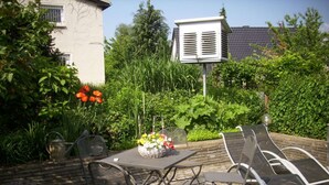 An outdoor patio with a table and chairs, surrounded by lush greenery and a white building in the background. - Apartment at the Knappensee in Gross Sarchen (Ebersbach-Neugersdorf)