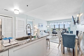 A modern kitchen with a marble countertop, a sink, and a dining area with a table and chairs.