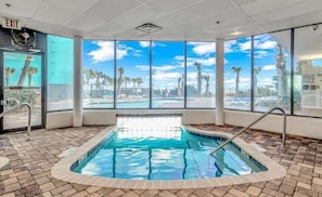 An indoor swimming pool with a clear view of palm trees and a blue sky through large windows.