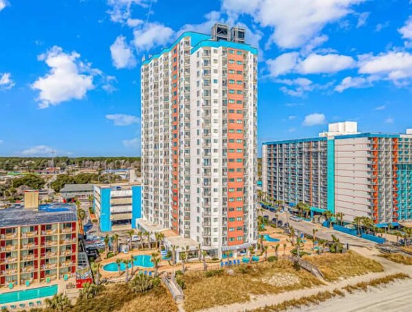 A high-rise hotel with multiple floors, a swimming pool, and a beach area.