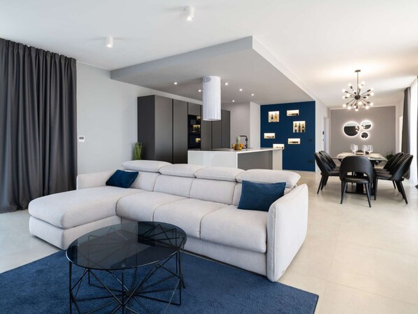 A modern living room with a sectional sofa, a glass coffee table, and a dining area with a chandelier.