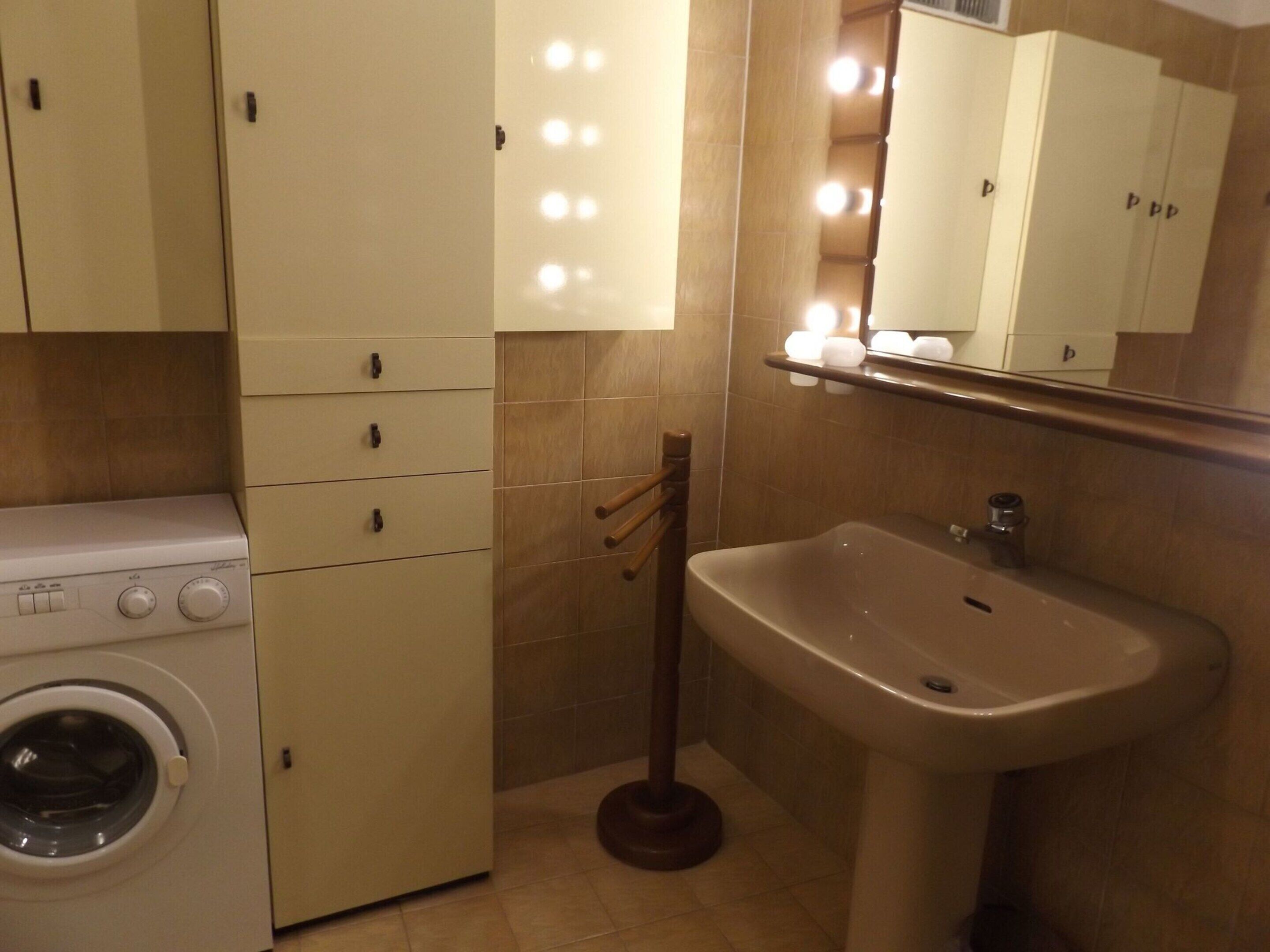 Un baño pequeño con lavadora, lavamanos y un espejo con iluminación.