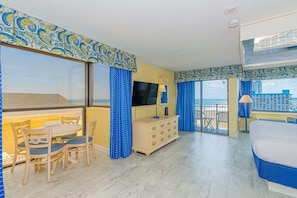 Camera d'albergo con balcone, zona pranzo con sedie e tavolo, un letto e una televisione.