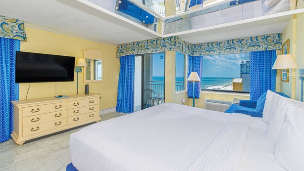 Een hotelkamer met een groot bed, een televisie, een dressoir en een balkon met uitzicht op zee.
