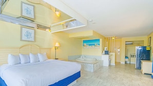 Een hotelkamer met een groot bed, een badkamer met een bad, een koelkast en een schilderij van een strand.