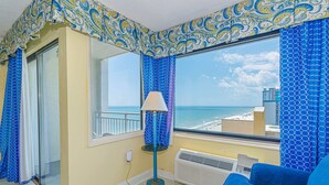 Een kamer met uitzicht op zee, een blauwe bank, een staande lamp en kamer met behang.