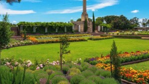 Un jardín con un monumento alto, céspedes bien cuidados y una variedad de coloridas parterres.