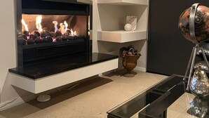 Una sala de estar moderna con chimenea, estanterías blancas y una mesa de centro de vidrio.