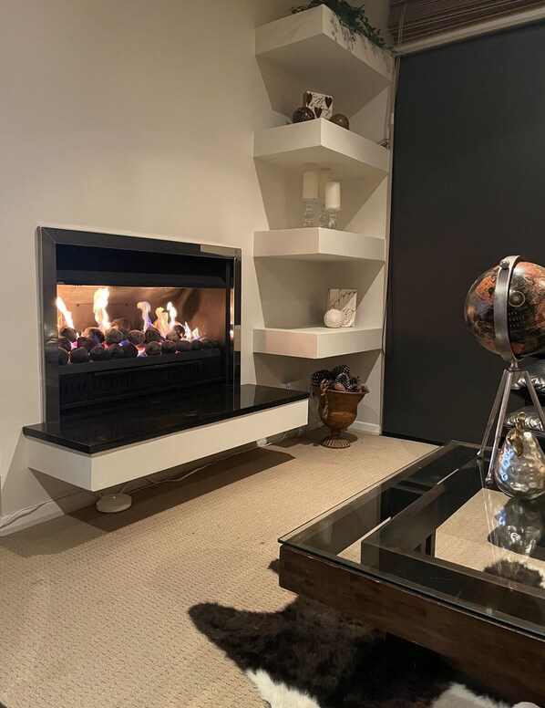 A modern living room with a fireplace, white shelving, and a glass coffee table.