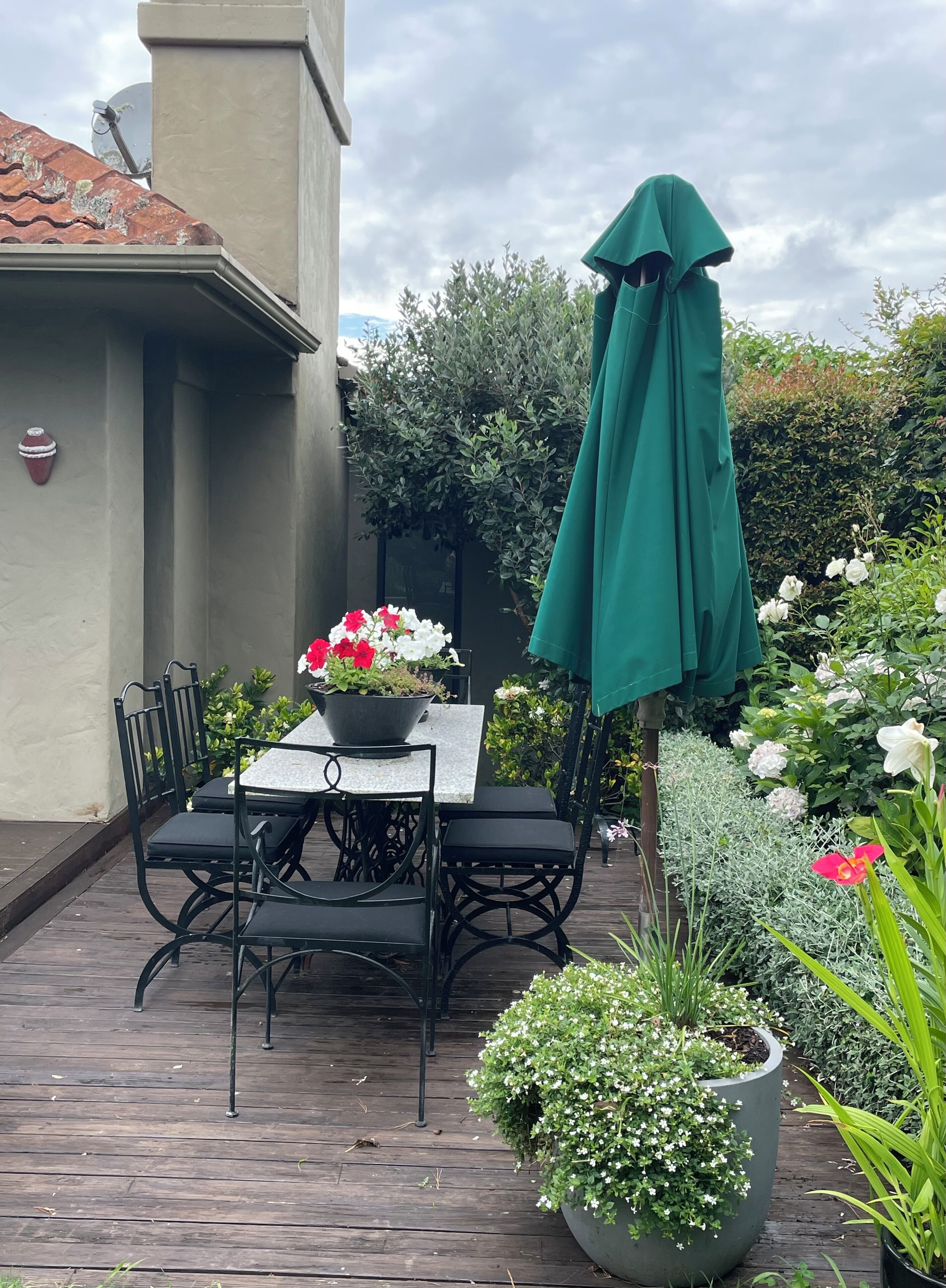 Um pátio com mesa, cadeiras, um guarda-sol verde e plantas em vasos.