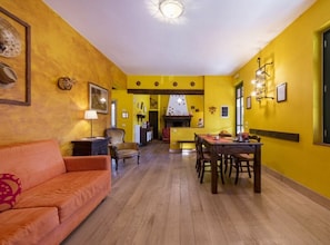 A room with a wooden floor, yellow walls, a dining table with chairs, a sofa, and a fireplace.
