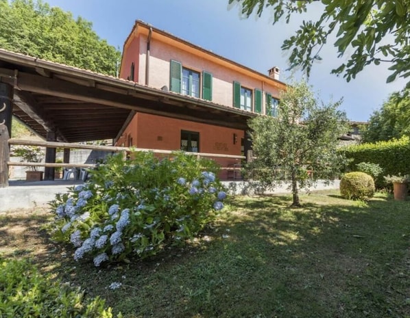 A two-story building with a sloped roof, green shutters, and a covered porch.