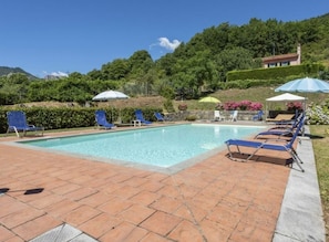 A rectangular swimming pool with blue lounge chairs and umbrellas on the right side.