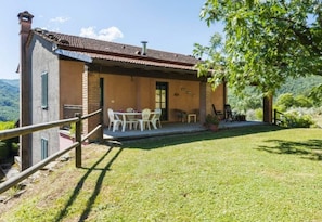 A rustic house with a tiled roof, a small patio with a table and chairs, and a grassy yard.