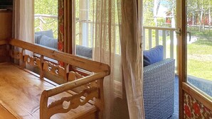 Un banco de madera con asiento y respaldo acolchados, ubicado cerca de una ventana que ofrece vistas a una terraza de madera y follaje exterior.
