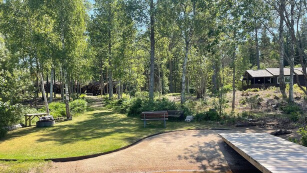 Un espacio natural al aire libre con una terraza de madera, un camino de grava y una pequeña fuente de agua.