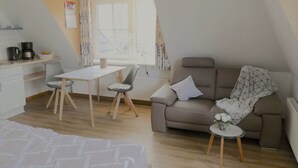 A modern, compact living space with a kitchenette, a dining area, a sofa, and a small round table. - Kille Family - Attic (St. Peter-Ording)