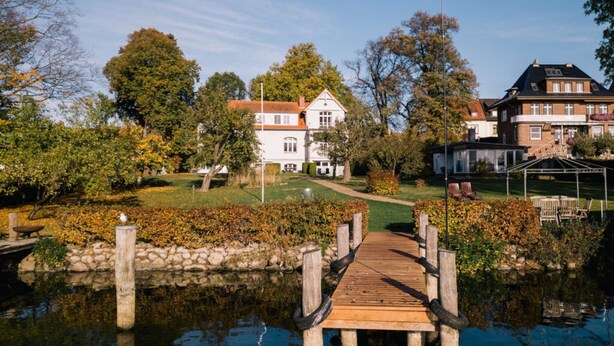Une jetée en bois menant à une maison dotée d’un jardin et d’un étang.