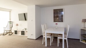 Une pièce moderne et bien éclairée, avec une table à manger, des chaises, un fauteuil à bascule, un téléviseur et un tableau accroché au mur.