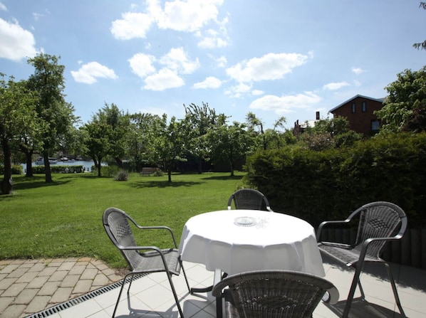 An outdoor patio with a round table and four chairs, surrounded by a well-maintained lawn and trees.