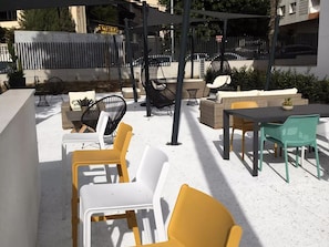 An outdoor seating area with yellow and white chairs, a table, and a pergola providing shade.